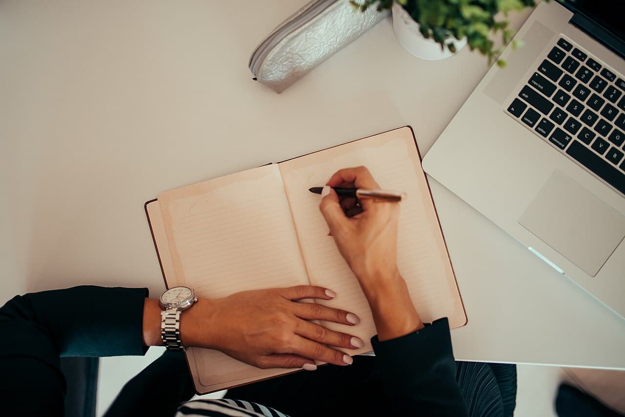 ノートパソコンを使いながらノートに手書きでメモを取っている人の手元(生成AIの独学を象徴する説明用写真)